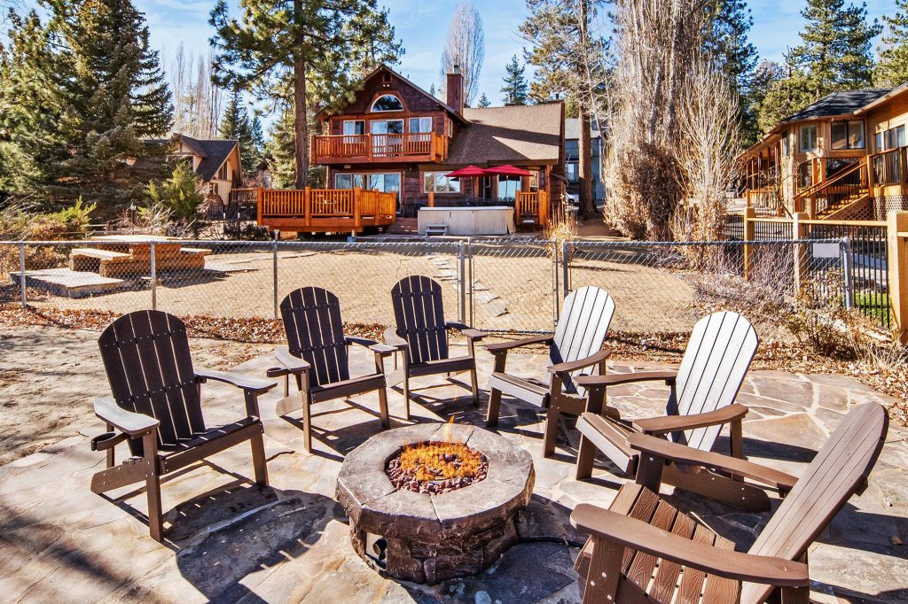 Outdoor deck with dining table, chairs, hot tub, and scenic view of lake and trees.