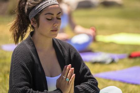 A woman with a grey headband and a black sweater meditating with her hands in prayer pose at a yoga event in Big Bear.