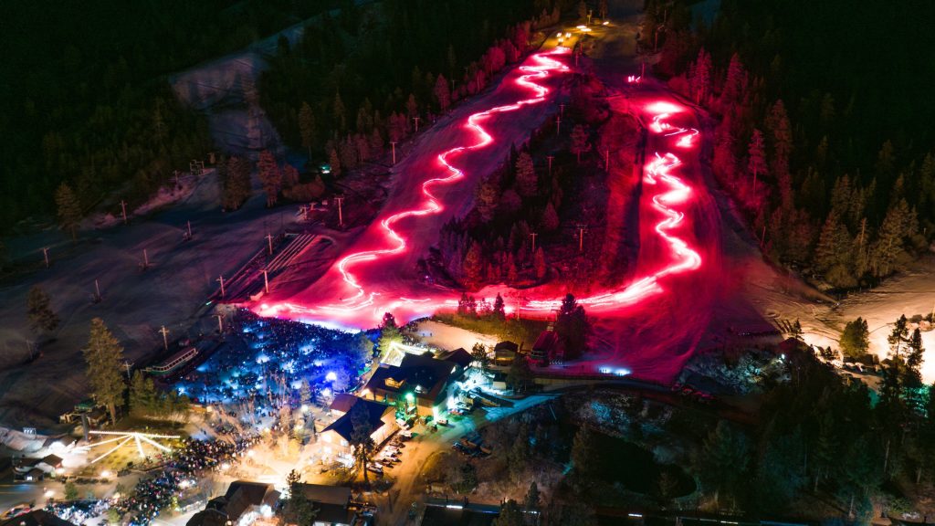 Aerial view of a glowing torchlight parade winding down the ski slopes at night during New Year's Eve