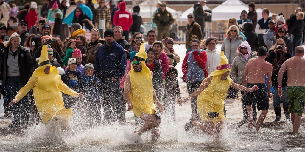 A group of people dressed in banana costumes runs into the freezing cold water at the Polar Plunge in Big Bear, with spectators watching from the snowy shoreline.