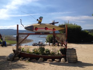 A giant fish sculpture with a cartoon fisherman on a boat at Big Bear Lake, promoting fishing and outdoor activities.