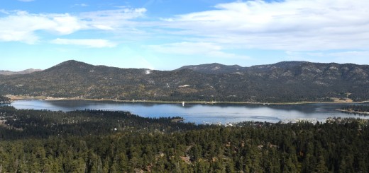 Scenic view of Big Bear Lake, surrounded by lush trees and majestic mountains under a clear blue sky.