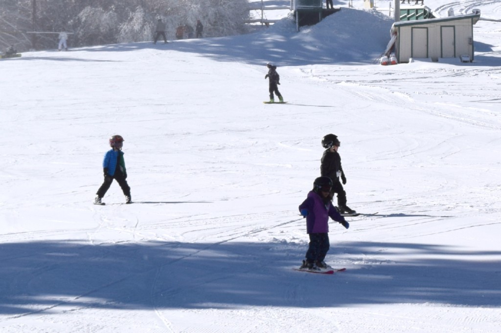 Several children in helmets and winter gear are skiing down a snowy slope at Big Bear