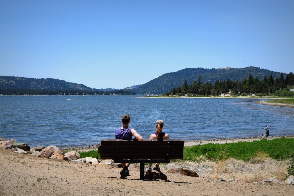 A man and a woman sit on a bench facing a lake in Big Bear.