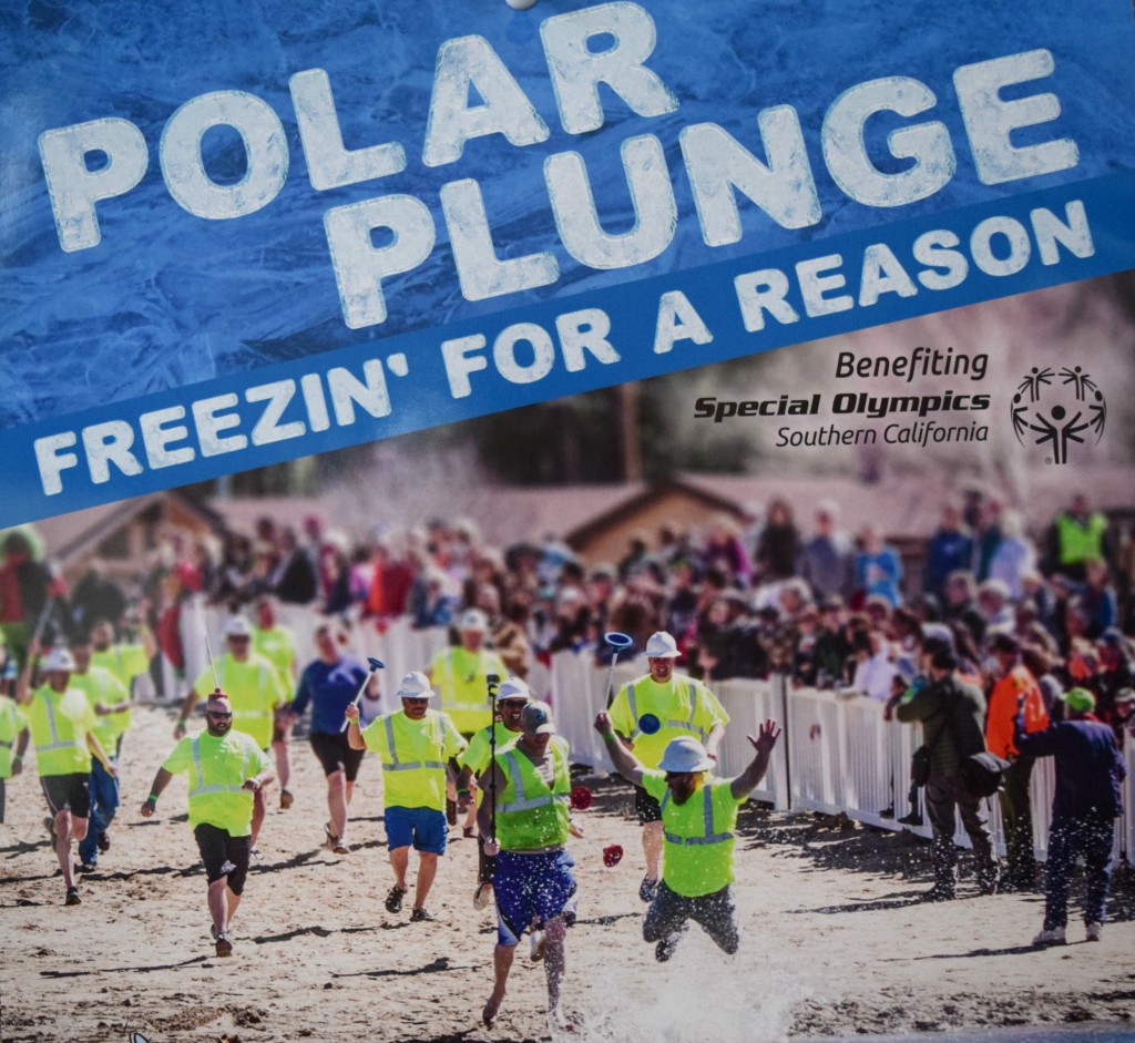 A group of people in bright green shirts and helmets run into the water at the Polar Plunge benefiting Special Olympics Southern California.
