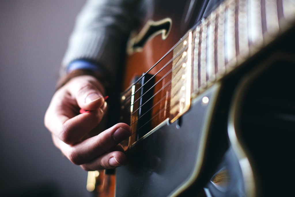 A close-up shows a hand strumming an electric guitar with a pick, depicting music at Big Bear.