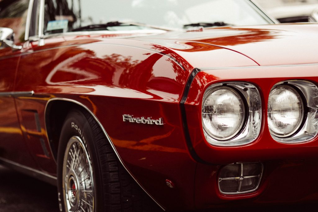 A close-up of the front of a shiny red vintage Pontiac Firebird car at the Big Bear car show.