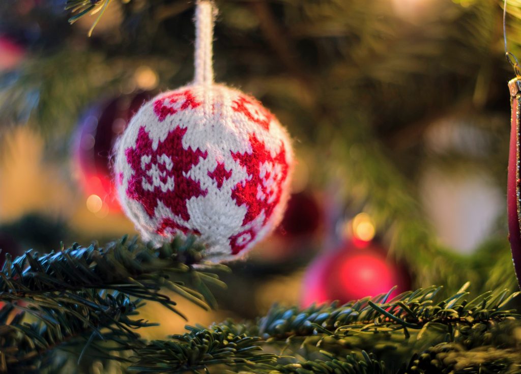A close-up shot of a white and red knitted ornament hanging on a Christmas tree.