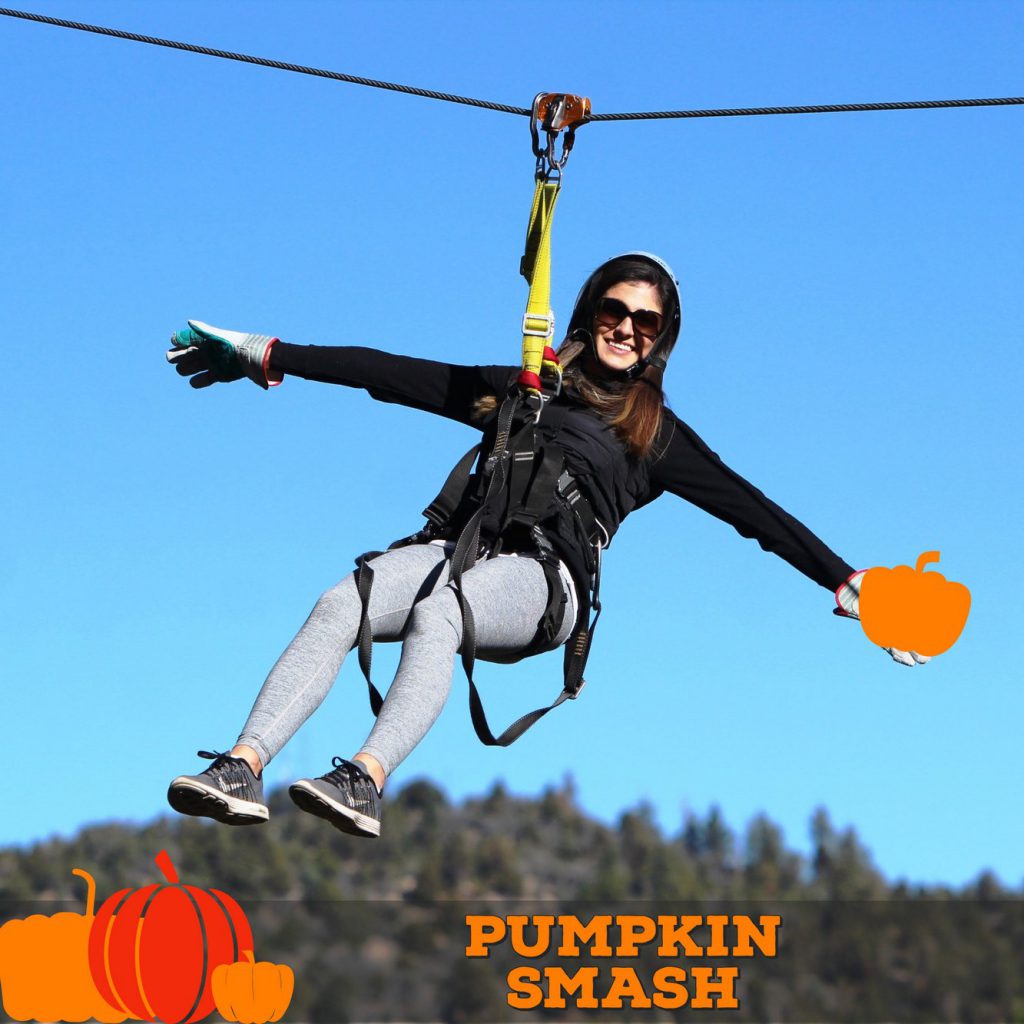 A woman smiling while ziplining with a pumpkin in her hand at a Pumpkin Smash event at Big Bear.