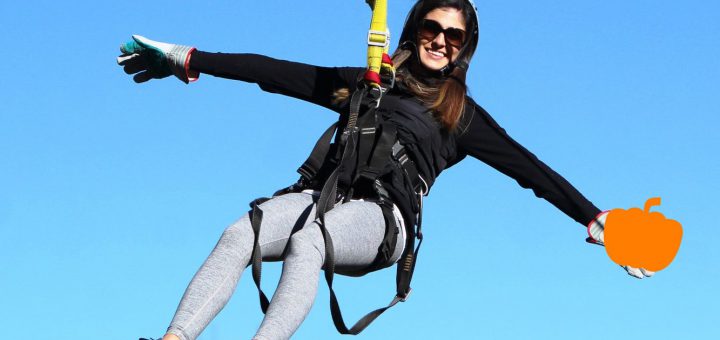 A woman smiling while ziplining with a pumpkin in her hand at a Pumpkin Smash event at Big Bear.