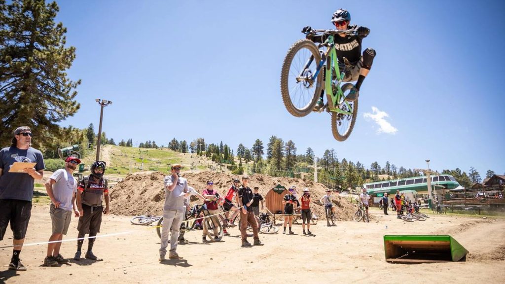Mountain biker performing a jump while spectators watch at a dirt track