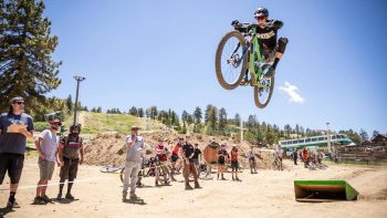 Mountain biker performing a jump while spectators watch at a dirt track