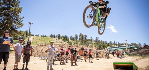 Mountain biker performing a jump while spectators watch at a dirt track