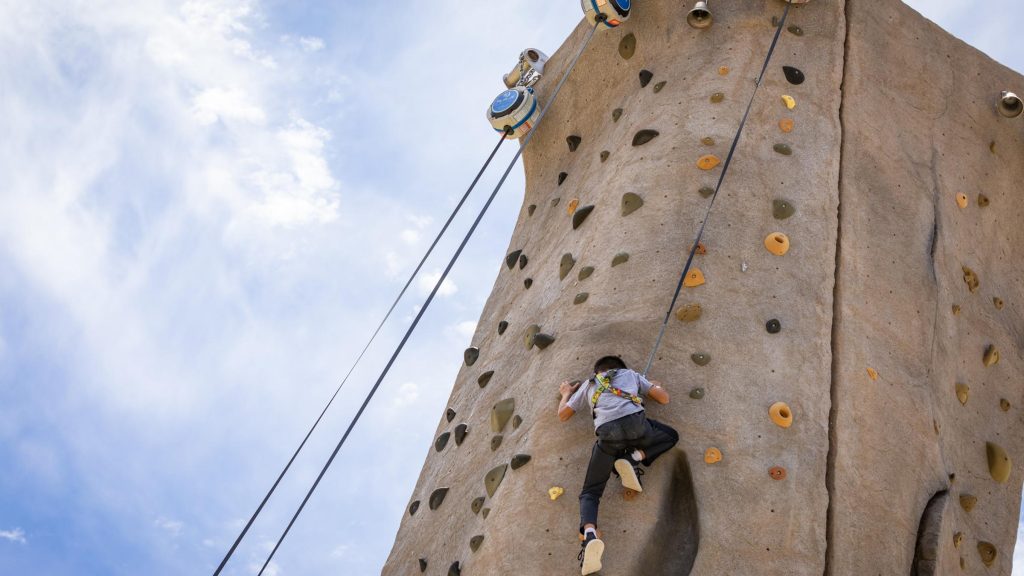 Person climbing an outdoor rock wall during an adventure activity under a clear sky.