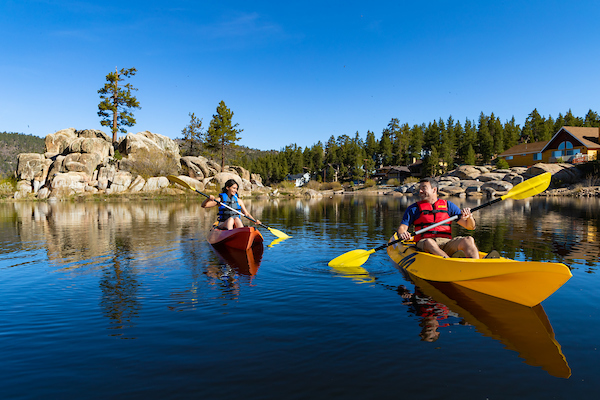 A couple in two separate kayaks paddling on a calm lake on a sunny day at Big Bear.