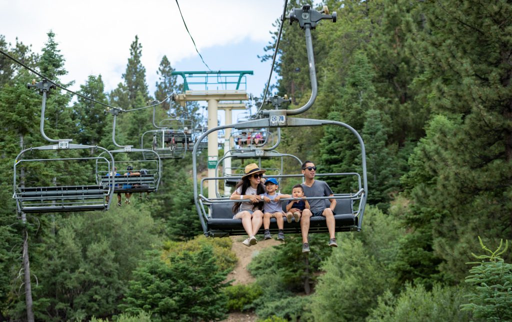 A family riding a ski lift in Big Bear, California, amidst beautiful forested mountains, enjoying a scenic winter experience.