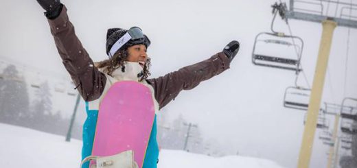 Girl with her snowboard raising her hands in the air under a chair lift