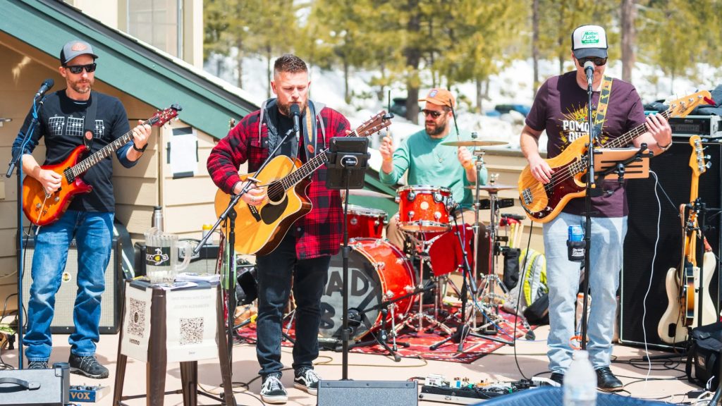 Live band performing outdoors at a mountain resort with trees and snow in the background