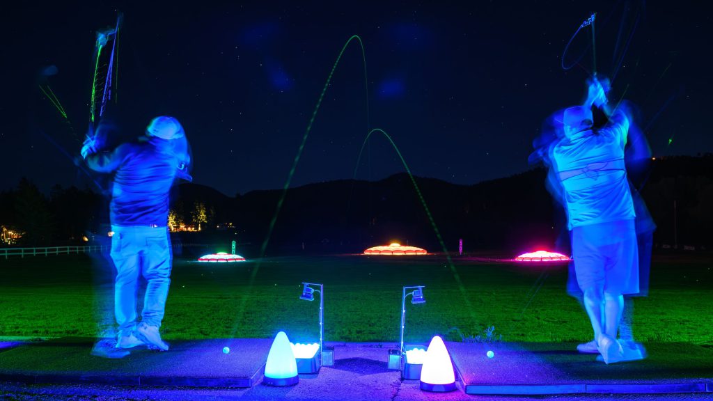 Golfers hitting glowing golf balls at a night driving range