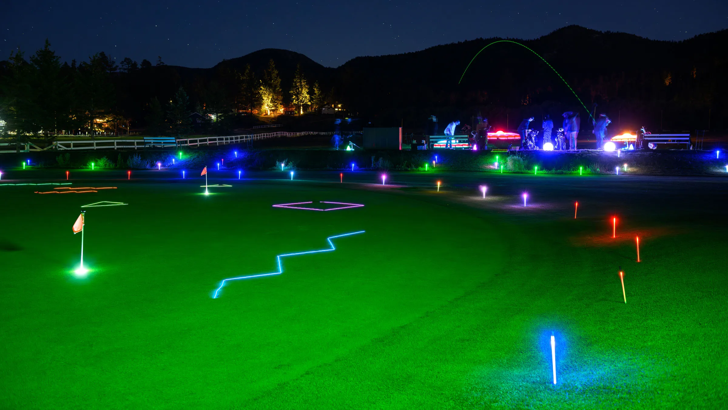 A vibrant night scene of golf at Big Bear, featuring illuminated fairways, glowing markers, and a golf ball soaring through the air.