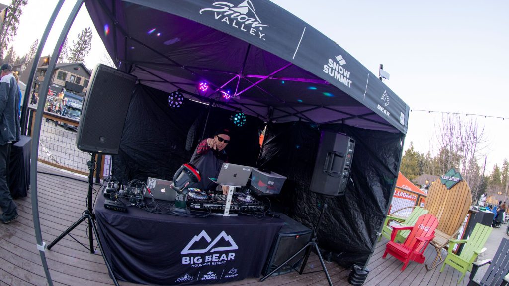 DJ performing at an outdoor employee party at Snow Summit with people and resort in the background.