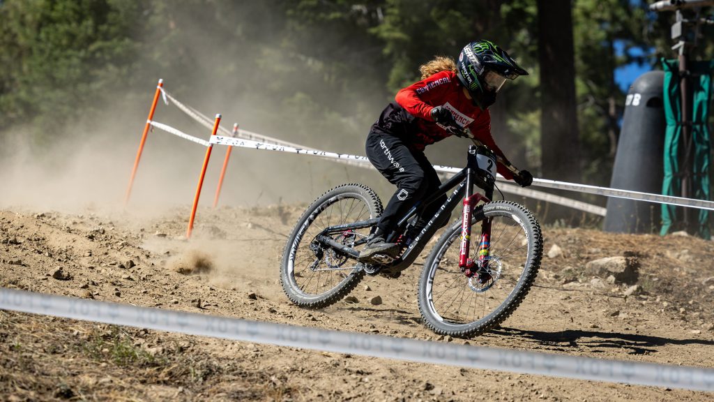 Female mountain biker in red jersey drifting during the Monster Energy Pro Downhill Series in Big Bear