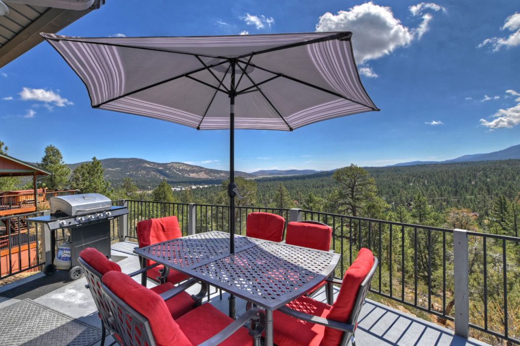 An outdoor patio in Big Bear with a table and chairs, a large umbrella, a grill, and a scenic mountain view in the background.