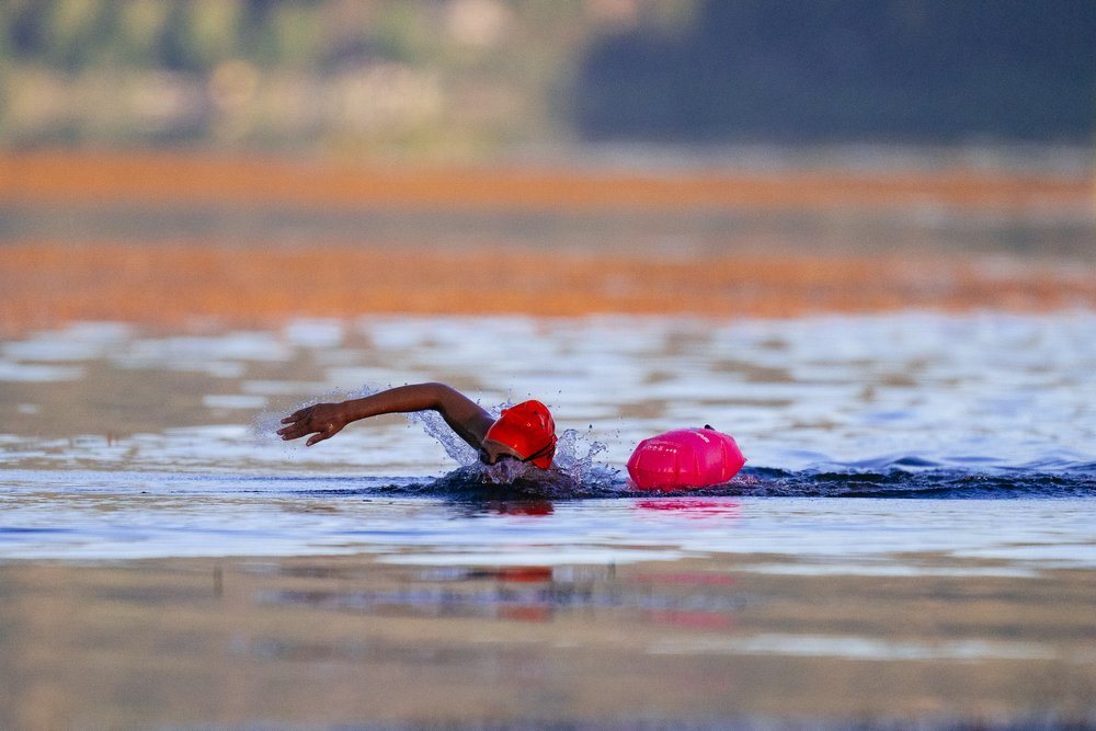 A person swimming in a lake with a pink flotation buoy nearby at the Big Bear LakeFest event.