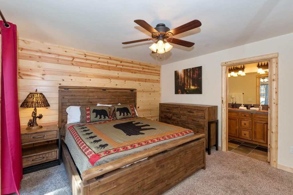A bedroom with a full-size bed and a wooden bunk bed, a wooden plank accent wall, and a ceiling fan in a cabin in Big Bear.