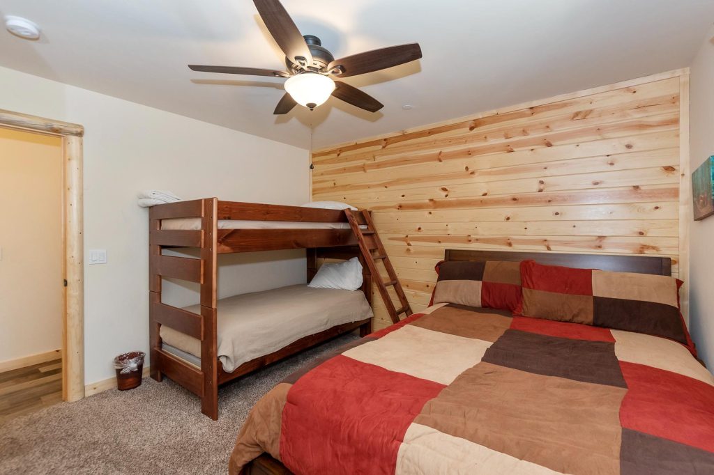 A bedroom with a full-size bed and a wooden bunk bed, a wooden plank accent wall, and a ceiling fan in a cabin in Big Bear.