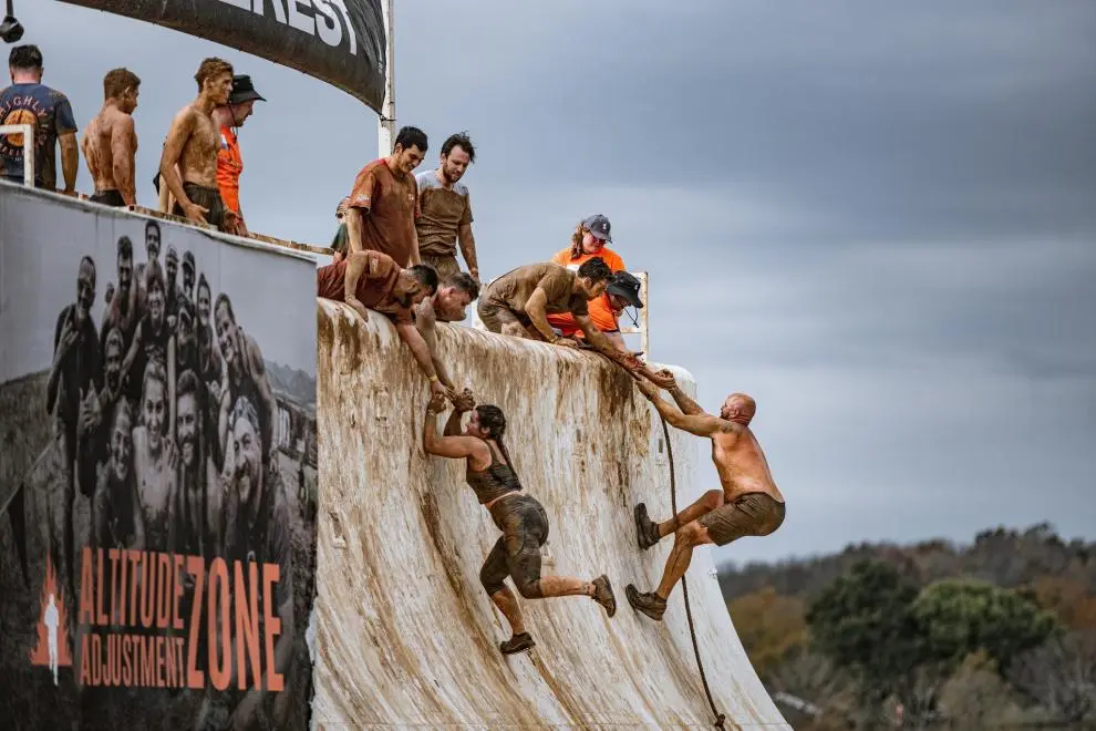 People covered in mud help each other up a steep, muddy wall at a Tough Mudder event in Big Bear.