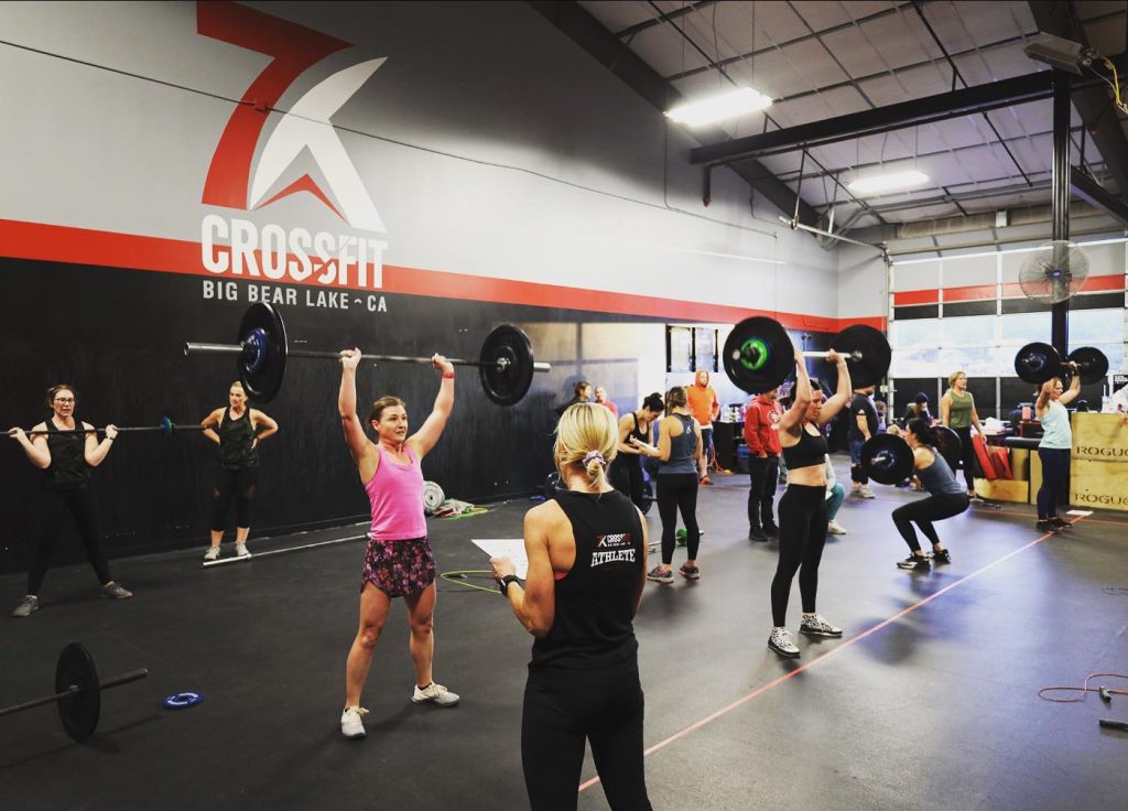 CrossFit group training session with athletes performing overhead barbell press inside a functional fitness gym