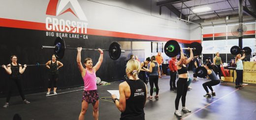 CrossFit group training session with athletes performing overhead barbell press inside a functional fitness gym
