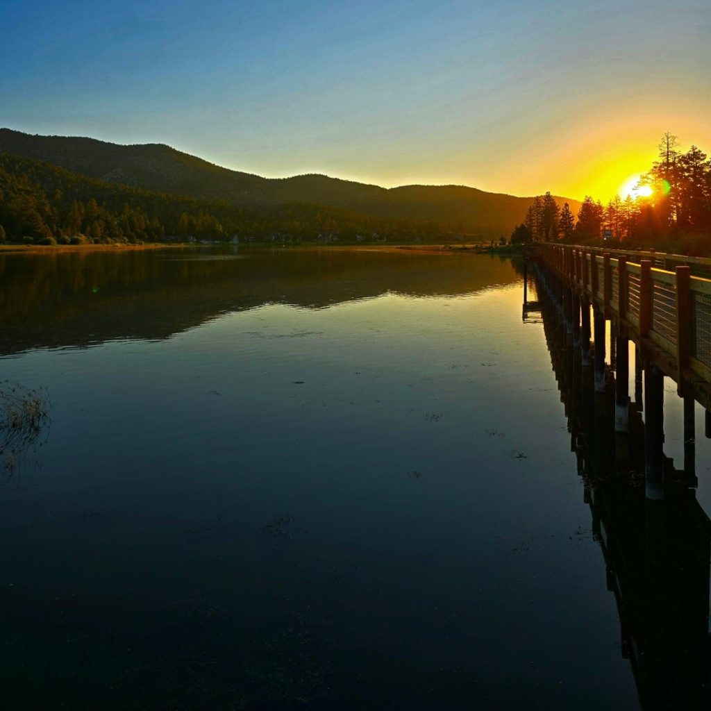 Sunset over Stanfield Marsh Boardwalk with reflections on the water and mountain silhouettes in the background.