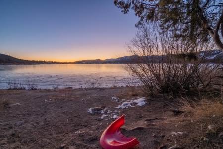 Sunset view of Big Bear Lake shoreline with a red kayak resting on the sandy beach
