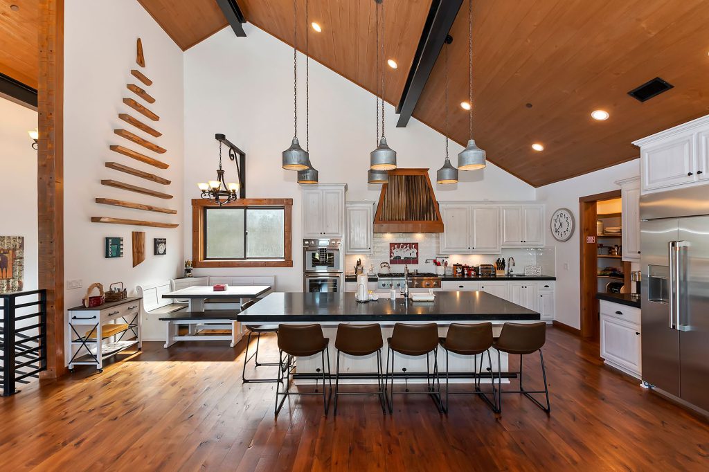 A modern cabin kitchen and dining area at Big Bear Studios with a large island, white cabinets, and a wood ceiling.