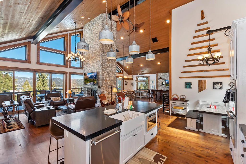 Spacious top-floor cabin interior featuring a modern kitchen, stone fireplace, vaulted ceiling, and scenic mountain lake views