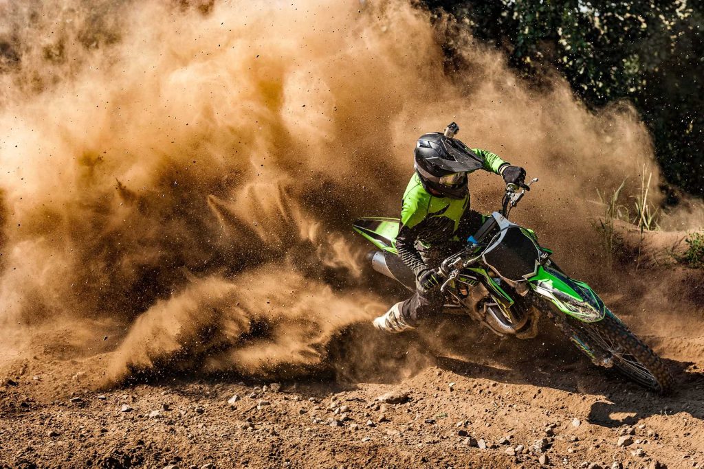 A dirt bike rider in green gear kicks up a large cloud of dust during a motocross race at Big Bear.