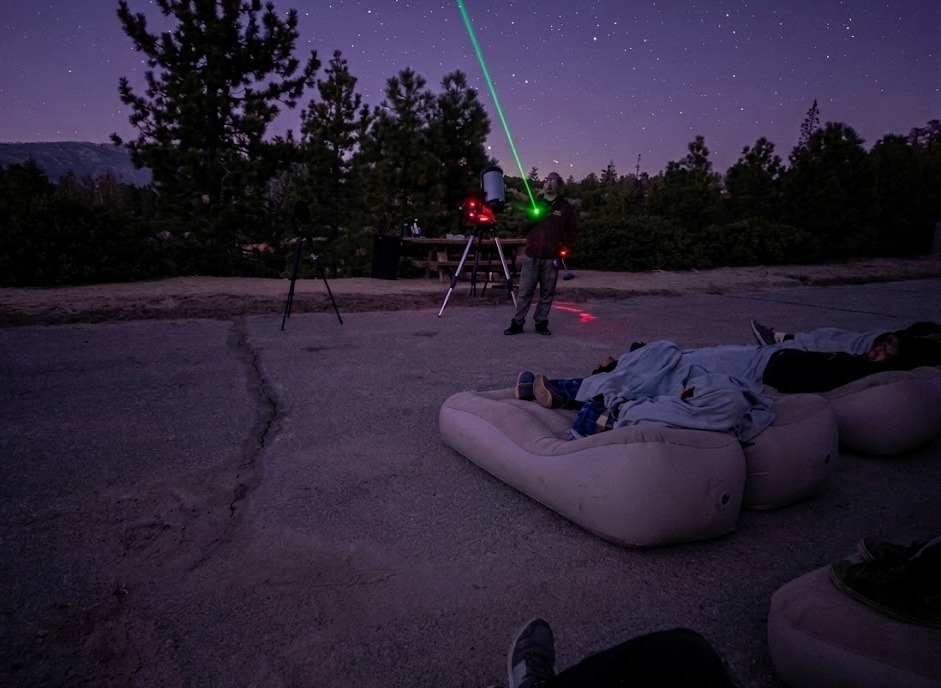 Visitors enjoying a stargazing experience under the night sky with a telescope and laser guide in Big Bear Lake.