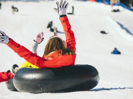 Snow Tubing at Alpine Slide in Big Bear with woman in orange coat going down a snow hill