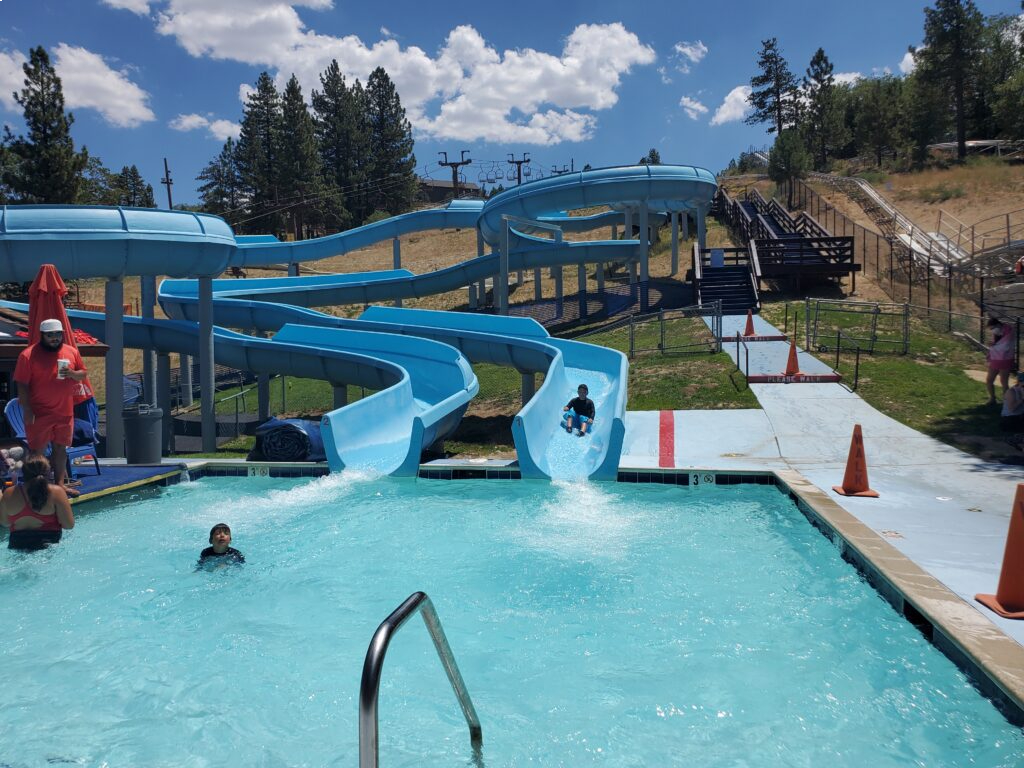 People enjoying outdoor water slides and splash pools at a mountain recreation area during summer