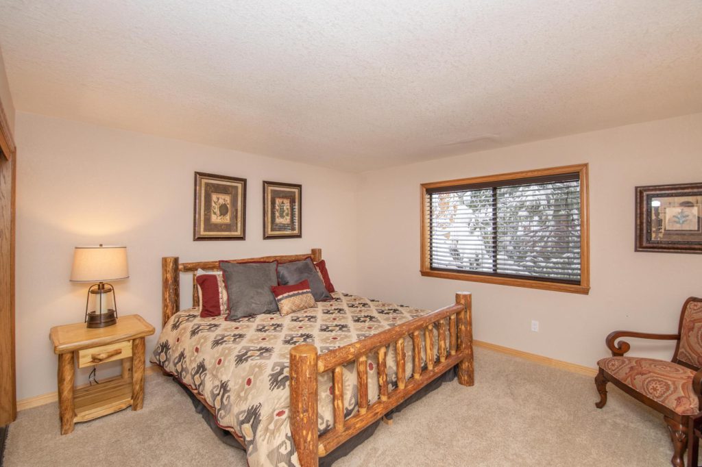 A bedroom with a bed with a wooden log frame, a nightstand, and framed artwork on the walls in Big Bear.