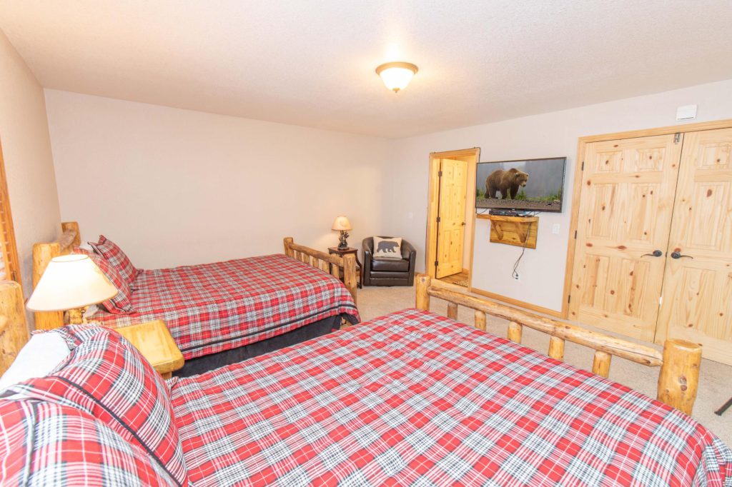 A bedroom with two twin beds featuring red and white plaid comforters, and a television mounted on the wall in Big Bear.