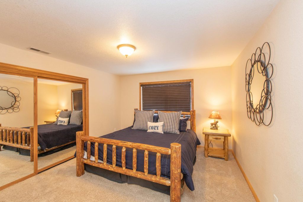 A cozy bedroom with a wooden log bed, mirrored closet doors, and a decorative mirror on the wall in Big Bear.