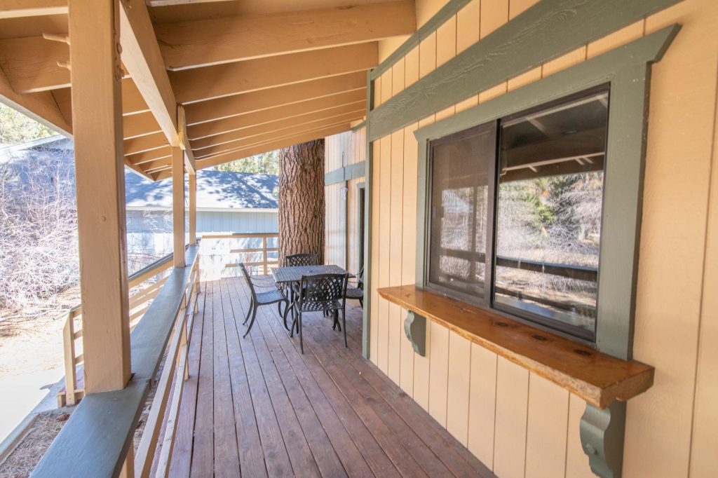 A wooden deck with a small table and two chairs, next to a cabin wall with a window, in Big Bear.