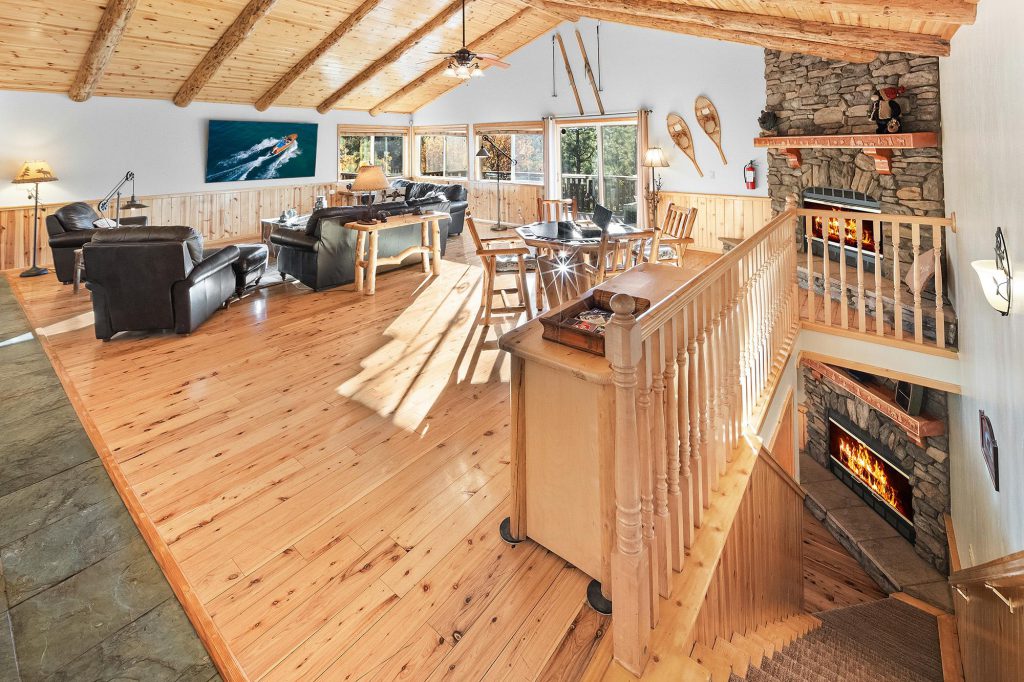 The interior of a large, two-story wooden cabin in Big Bear with a living area, dining table, and a fireplace.