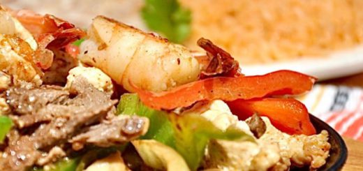 Grilled Shrimp, carne asada, green peppers, red peppers and grilled onions on a black plate with friend Spanish rice in the background