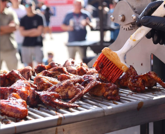 A person is basting chicken wings on a grill at Big Bear.
