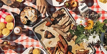 A high-angle shot of a table with a red and white checkered tablecloth, covered in various barbecue foods at Big Bear.