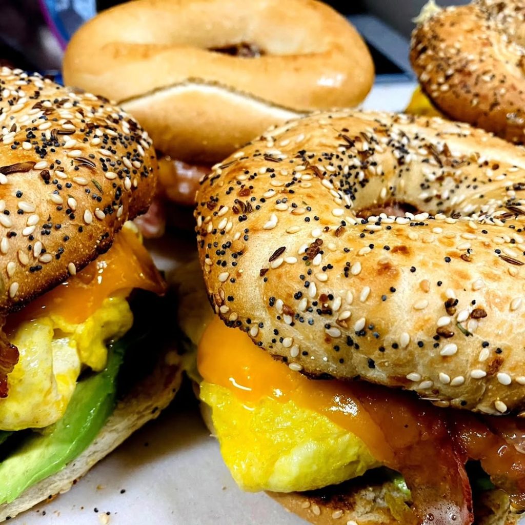 Close-up of breakfast bagel sandwiches filled with eggs, bacon, cheese, and fresh ingredients.